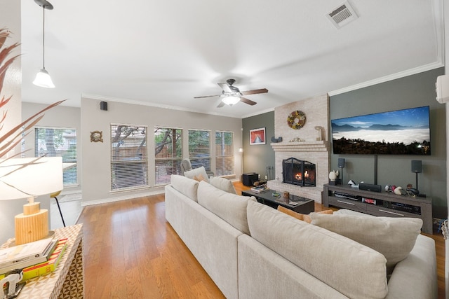 living room featuring a brick fireplace, light hardwood / wood-style flooring, ceiling fan, and ornamental molding