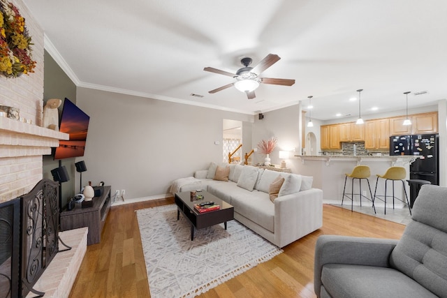 living room featuring a brick fireplace, ceiling fan, ornamental molding, and light hardwood / wood-style flooring