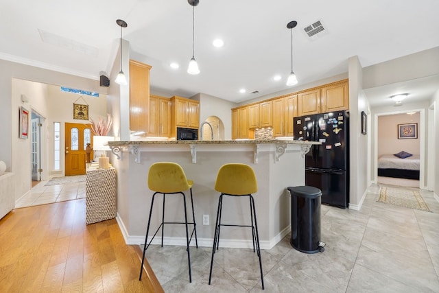 kitchen featuring light stone countertops, light brown cabinets, light hardwood / wood-style floors, and black appliances