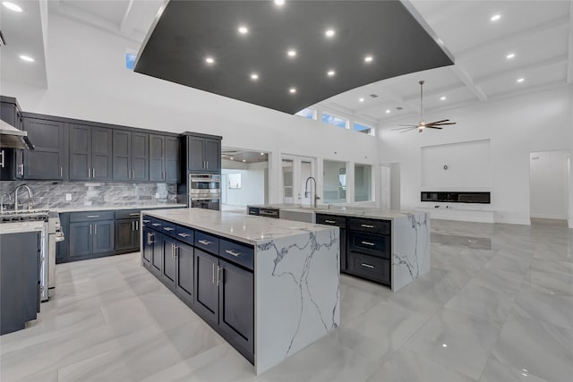 kitchen with decorative backsplash, a large island, light stone counters, and a high ceiling