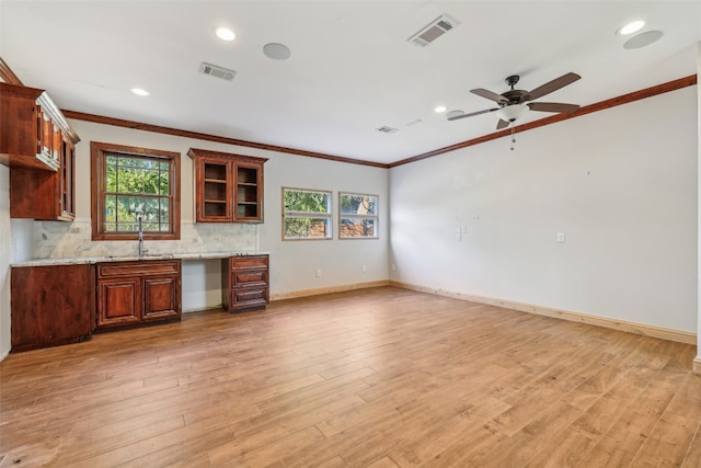 kitchen with light stone counters, ornamental molding, sink, and light hardwood / wood-style flooring