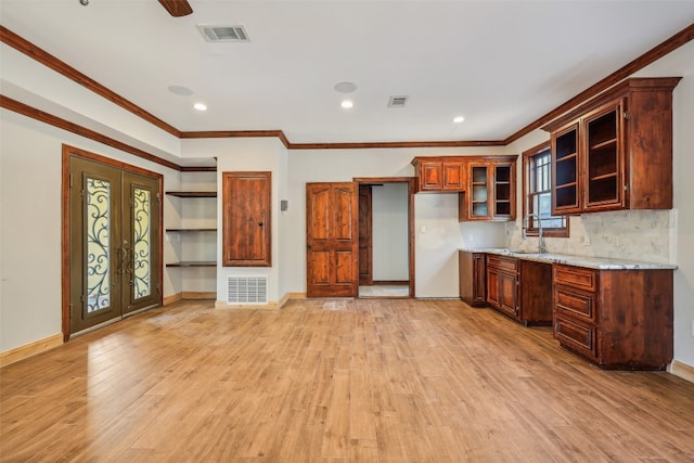 kitchen with light stone countertops, light hardwood / wood-style flooring, ornamental molding, and sink