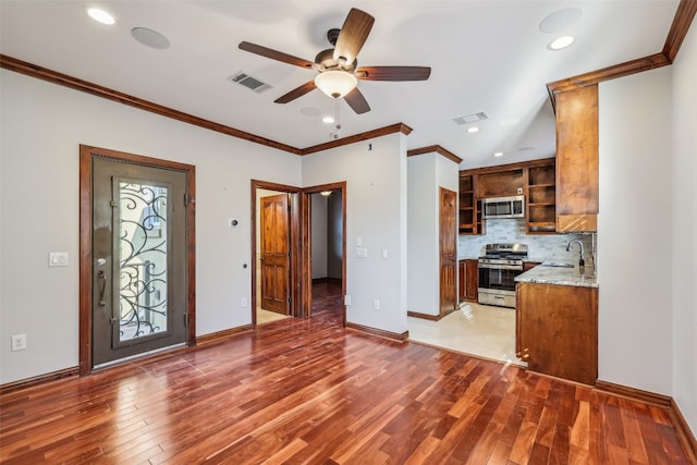 interior space with appliances with stainless steel finishes, hardwood / wood-style flooring, ceiling fan, and ornamental molding