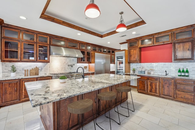 kitchen featuring decorative light fixtures, stainless steel appliances, an island with sink, and a tray ceiling