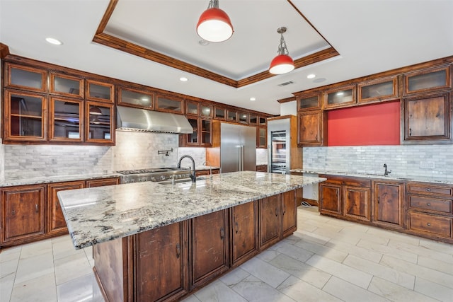 kitchen featuring pendant lighting, a raised ceiling, stainless steel appliances, and a center island with sink