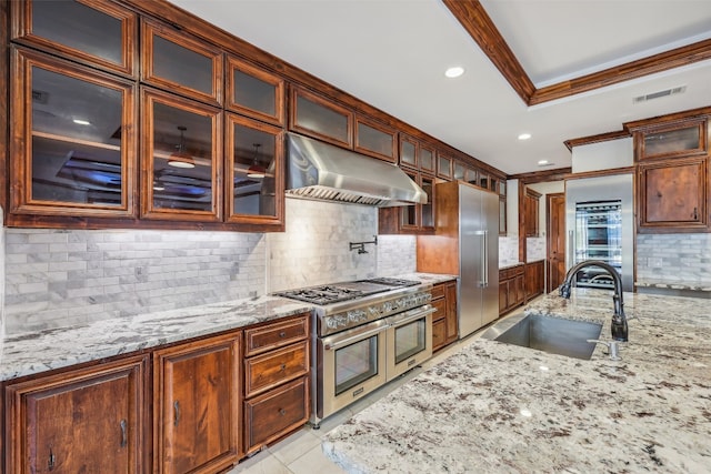 kitchen with light stone countertops, sink, premium appliances, ventilation hood, and decorative backsplash