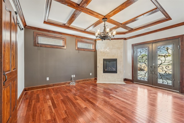 unfurnished living room with hardwood / wood-style floors, coffered ceiling, french doors, ornamental molding, and a chandelier