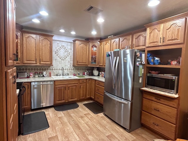 kitchen with appliances with stainless steel finishes, light wood-type flooring, tasteful backsplash, and sink