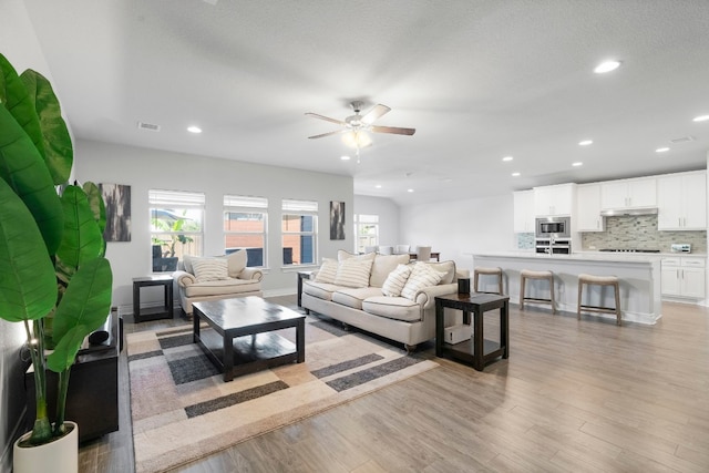 living room featuring a textured ceiling, light hardwood / wood-style floors, and ceiling fan