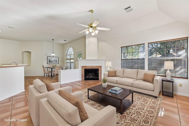 tiled living room featuring ceiling fan, a tile fireplace, a wealth of natural light, and lofted ceiling