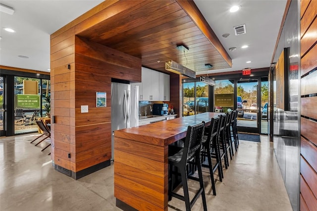 kitchen featuring butcher block counters, white cabinetry, stainless steel fridge, and wood walls