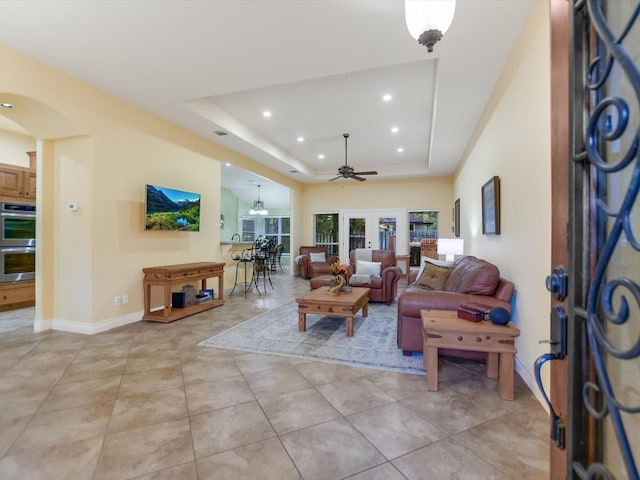 tiled living room featuring a raised ceiling, ceiling fan, and french doors