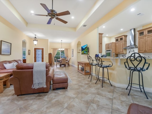 living room with ceiling fan with notable chandelier and a raised ceiling