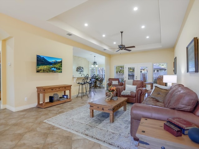 living room with a tray ceiling, french doors, and ceiling fan with notable chandelier