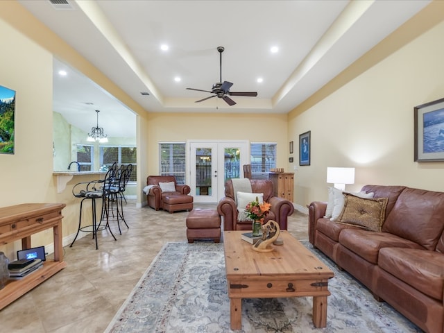 living room featuring french doors, ceiling fan with notable chandelier, and a tray ceiling