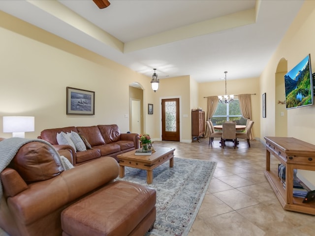 tiled living room with a raised ceiling and ceiling fan with notable chandelier