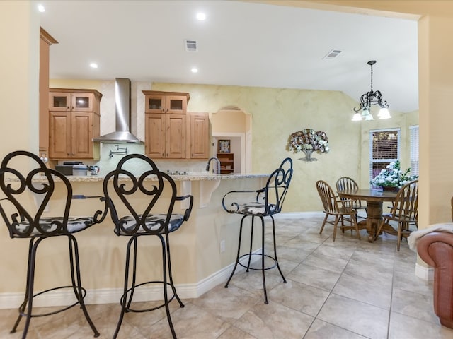 kitchen with hanging light fixtures, wall chimney range hood, light stone counters, a notable chandelier, and kitchen peninsula