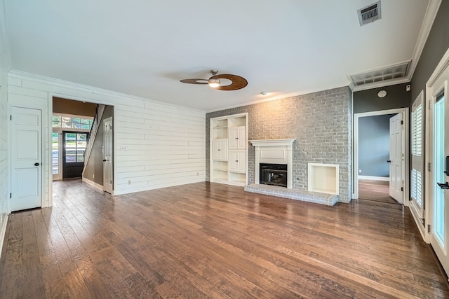 unfurnished living room featuring dark wood-type flooring, a brick fireplace, ceiling fan, ornamental molding, and brick wall