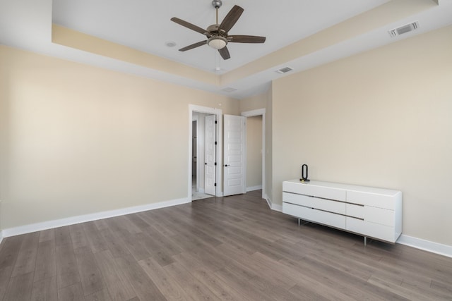 unfurnished bedroom with a raised ceiling, ceiling fan, and wood-type flooring