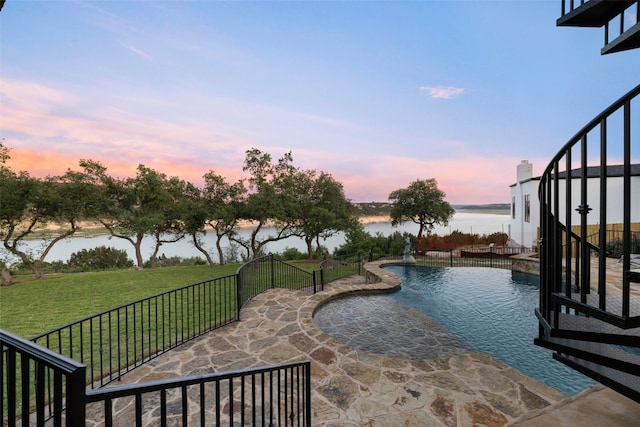 pool at dusk featuring a patio area, a water view, and a yard