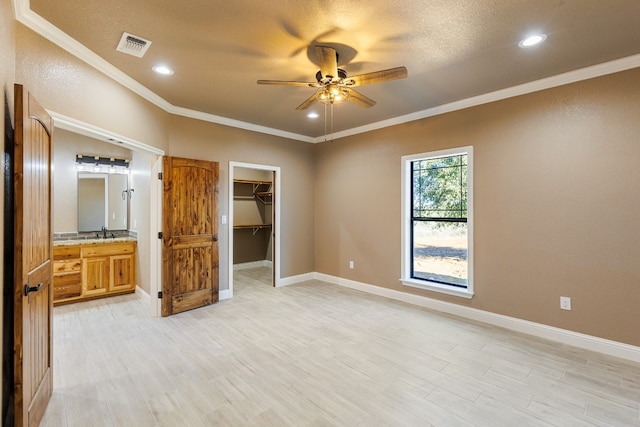 unfurnished bedroom with ensuite bathroom, a walk in closet, ceiling fan, ornamental molding, and light hardwood / wood-style floors