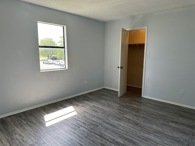 unfurnished bedroom featuring dark hardwood / wood-style floors, a spacious closet, a textured ceiling, and a closet