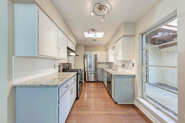 kitchen with sink, light wood-type flooring, appliances with stainless steel finishes, tasteful backsplash, and white cabinetry