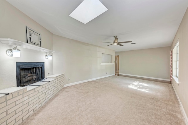 unfurnished living room with a skylight, ceiling fan, light colored carpet, and a brick fireplace