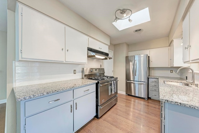 kitchen featuring appliances with stainless steel finishes, light stone counters, sink, light hardwood / wood-style floors, and white cabinetry