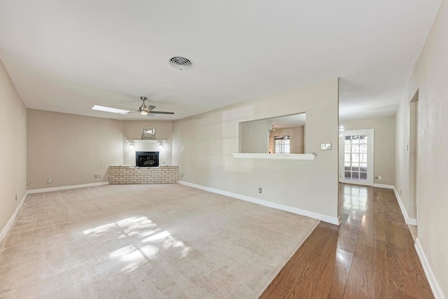 unfurnished living room featuring wood-type flooring, a brick fireplace, and ceiling fan