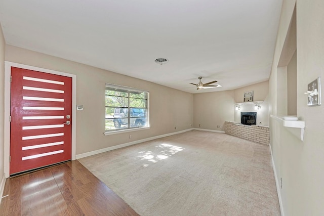 unfurnished living room with a wood stove, ceiling fan, and light wood-type flooring