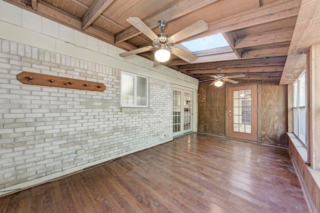 unfurnished room featuring hardwood / wood-style flooring, beam ceiling, brick wall, and a skylight