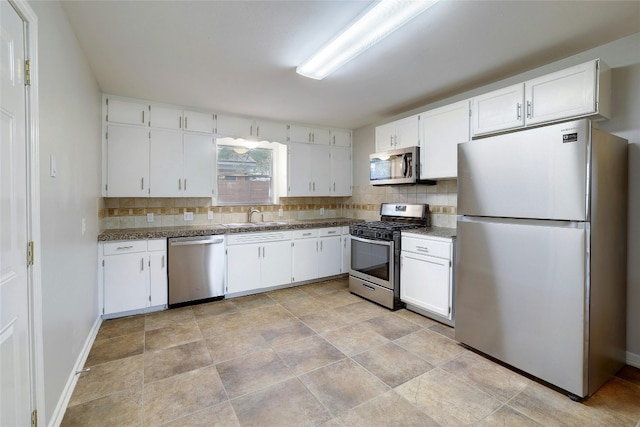 kitchen with appliances with stainless steel finishes, tasteful backsplash, dark stone counters, sink, and white cabinets