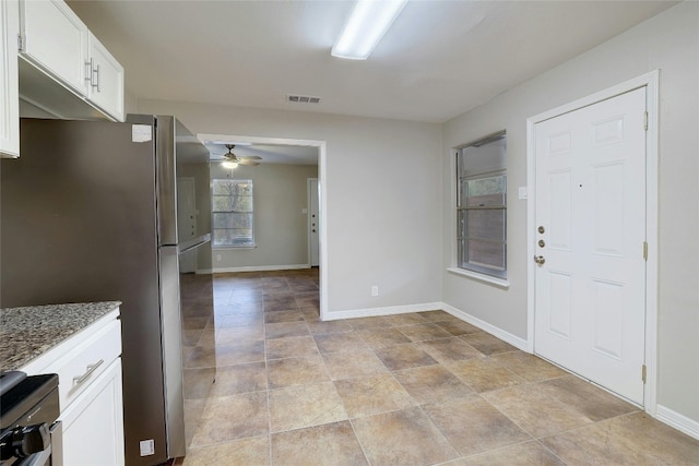 kitchen featuring white cabinets, ceiling fan, stainless steel refrigerator, and dark stone counters