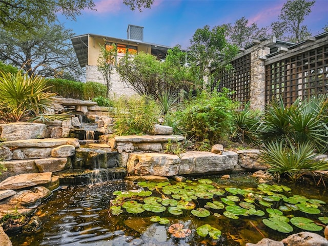 yard at dusk featuring a garden pond