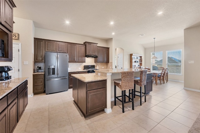 kitchen with decorative backsplash, stainless steel fridge, dark brown cabinetry, black gas range, and a center island