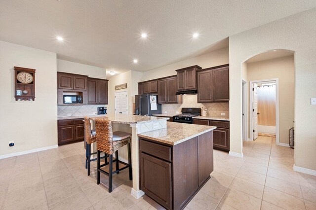 19316 Chayton Cir, Pflugerville, TX 78660 - kitchen with black appliances, arched walkways, backsplash, dark brown cabinets, and a breakfast bar