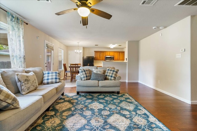 living room with ceiling fan with notable chandelier and dark hardwood / wood-style floors