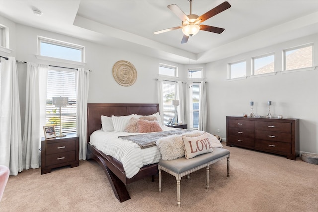 bedroom with ceiling fan, light colored carpet, a tray ceiling, and multiple windows