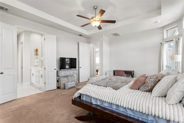 bedroom featuring ceiling fan, a raised ceiling, light carpet, and ensuite bath