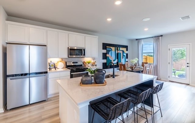 kitchen featuring light hardwood / wood-style flooring, stainless steel appliances, an island with sink, and white cabinets