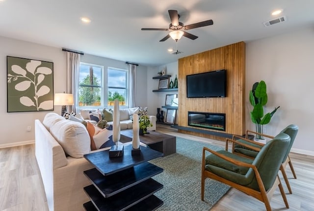 living room featuring ceiling fan, a large fireplace, and light wood-type flooring