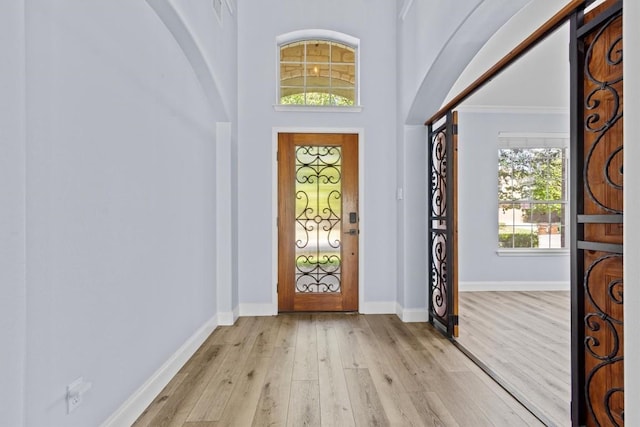 foyer entrance with a towering ceiling, light hardwood / wood-style flooring, and crown molding