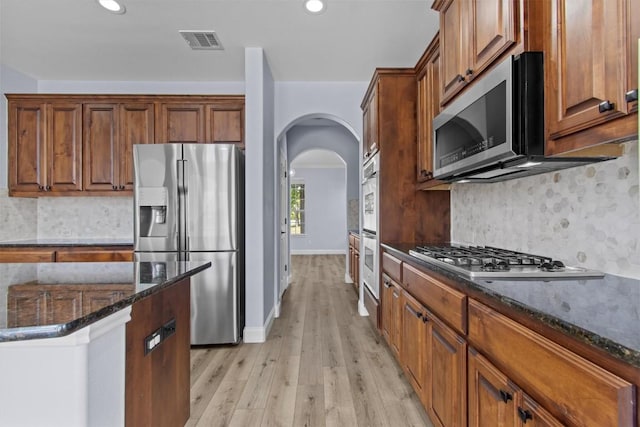 kitchen featuring backsplash, stainless steel appliances, light hardwood / wood-style floors, and dark stone countertops