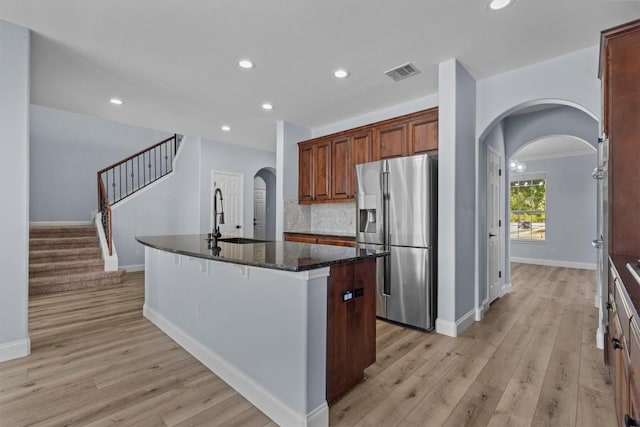 kitchen featuring light wood-type flooring, sink, a center island with sink, dark stone countertops, and stainless steel fridge with ice dispenser