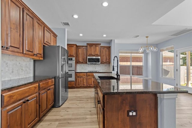 kitchen featuring appliances with stainless steel finishes, backsplash, sink, a notable chandelier, and an island with sink