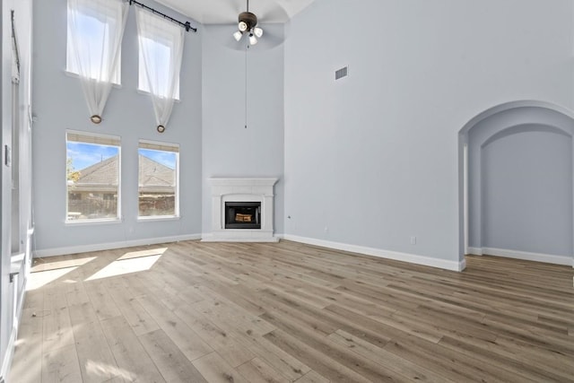 unfurnished living room with ceiling fan, plenty of natural light, and a high ceiling