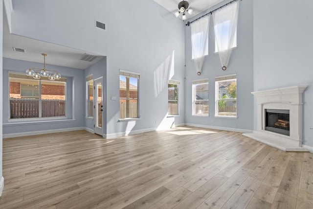 unfurnished living room with a towering ceiling, light hardwood / wood-style floors, and an inviting chandelier