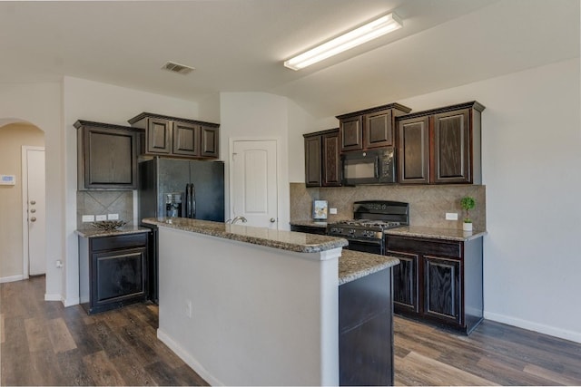 kitchen with backsplash, black appliances, a center island with sink, dark hardwood / wood-style flooring, and dark brown cabinetry