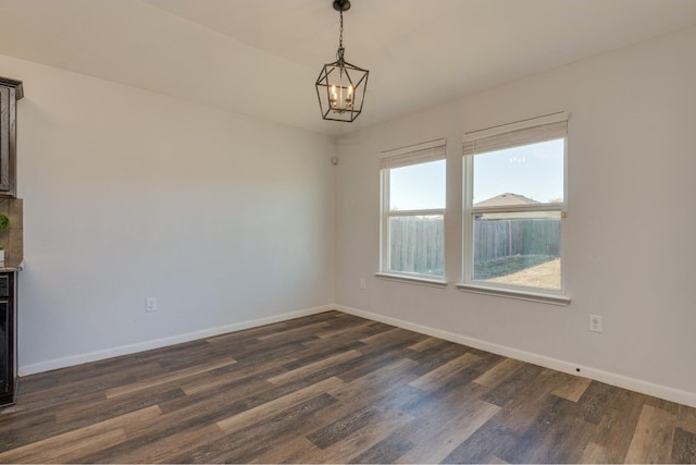 spare room with a chandelier and dark wood-type flooring